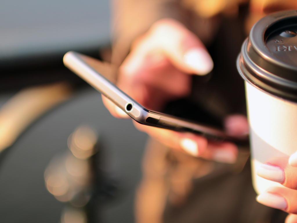 Person holding a phone and coffee